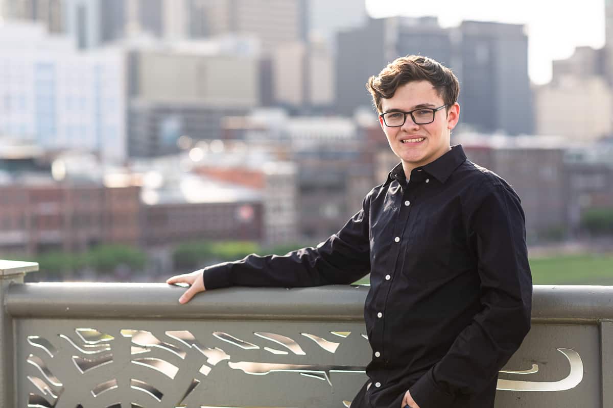 senior boy stands on bridge with skyline behind